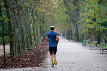Runner corriendo en footing entre &aacute;rboles del parque con hojas ca&iacute;das de oto&ntilde;o en suelo