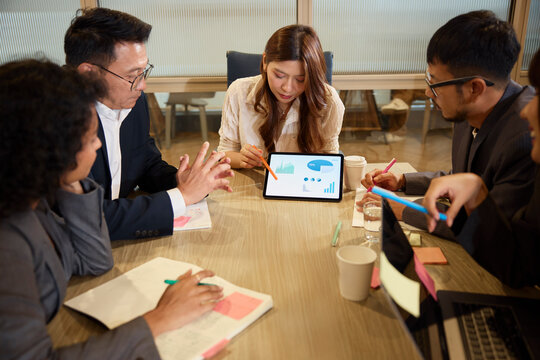 Businesswoman explaining diagrams on digital tablet to team in meeting room