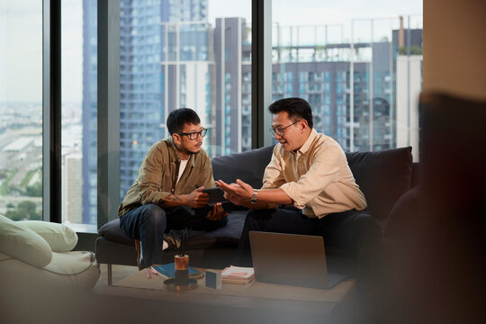 Young businessman listening to manager planning strategies while sitting on sofa