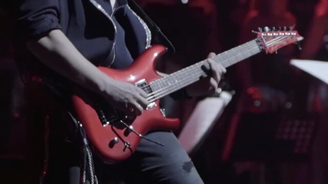 Guitarist intently focused on playing striking electric guitar under subtle stage lighting. Live concert setting emphasizes joy of music