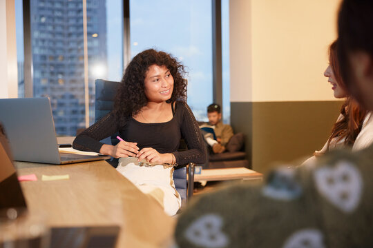 Smiling female manager listening to colleague while sitting on chair in office