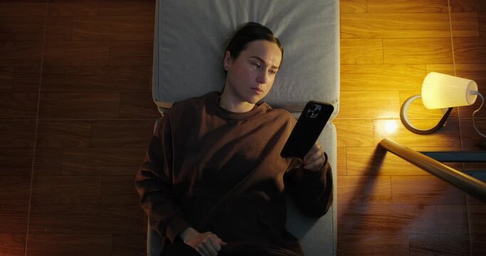 Top View of a Woman Lying on a Chaise Lounge and Scrolling on Her Smartphone at Night