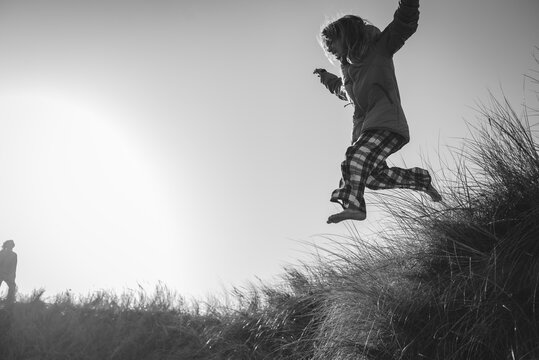 Black and white image of carefree girl jumping on grass while enjoying leisure time with father