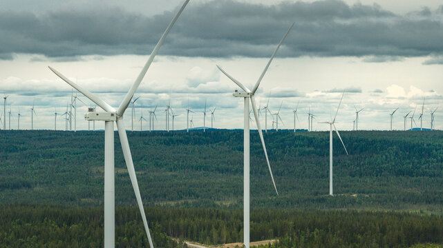 Wind turbines amidst trees under cloudy sky
