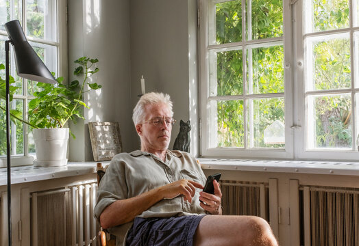 Senior man scrolling smart phone while sitting on chair at home