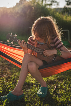 Girl playing guitar while sitting in hammock at backyard on sunny day