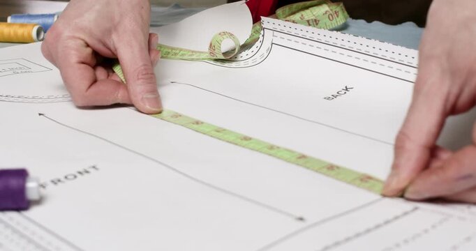 Professional man tailor aligns measuring tape with printed pattern lines. Skilled craftsman uses tape measure to check dimensions to avoid sizing errors