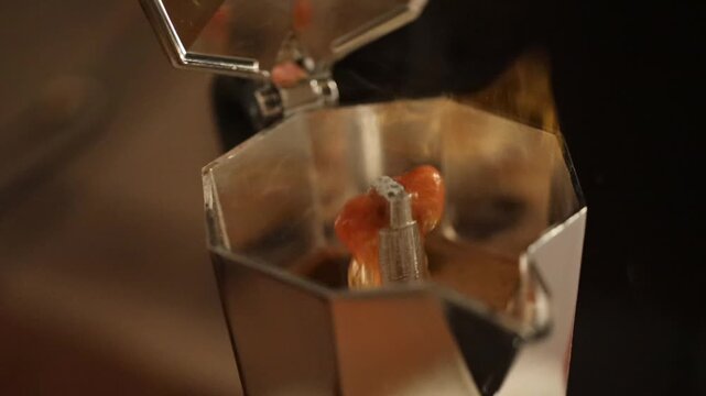 A hand opens a moka pot to reveal freshly boiling coffee inside.
