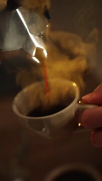 Fresh coffee is poured from a moka pot into a cup in a home kitchen.