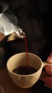 Fresh coffee is poured from a moka pot into a cup in a home kitchen.