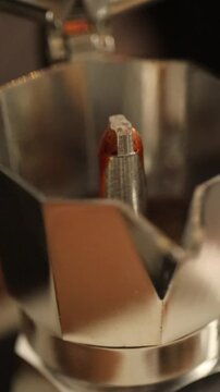 A hand opens a moka pot to reveal freshly boiling coffee inside.