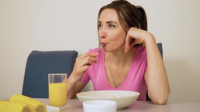 Woman biting dumpling with fork while sitting at dining table. Girl eating pelmeni slowly while looking aside. Female tasting ravioli during lunch at home kitchen