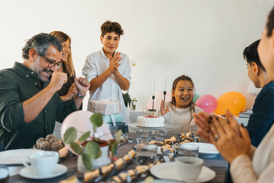 Cheerful family clapping for girl during birthday celebration at home