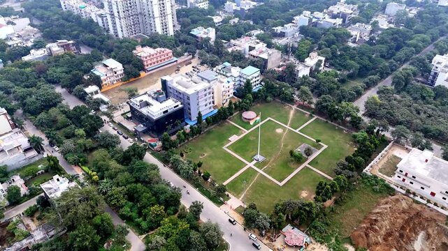Aerial view of a National Flag plaza in Greater Noida, with a towering tricolor rising from a landscaped square, surrounded by tree-lined streets and civic buildings.