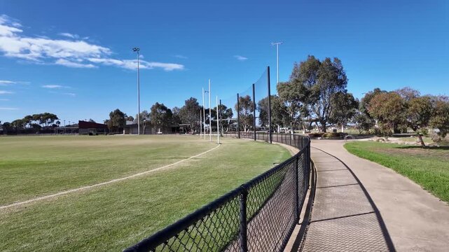 A suburban sports field in Australia featuring an Australian rules football oval with tall goal posts, boundary fencing. Community recreation facilities, local sports infrastructure in a neighbourhood