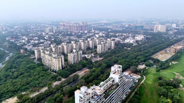 Aerial view of high-rise towers under construction in Greater Noida, with cranes piercing a smog-filled skyline, reflecting rapid urban growth amid visible air pollution.