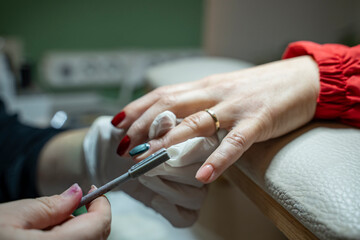 In a beauty salon, a manicurist uses a magnet to apply cat-eye green nail polish to a customer's hand (stock photo).