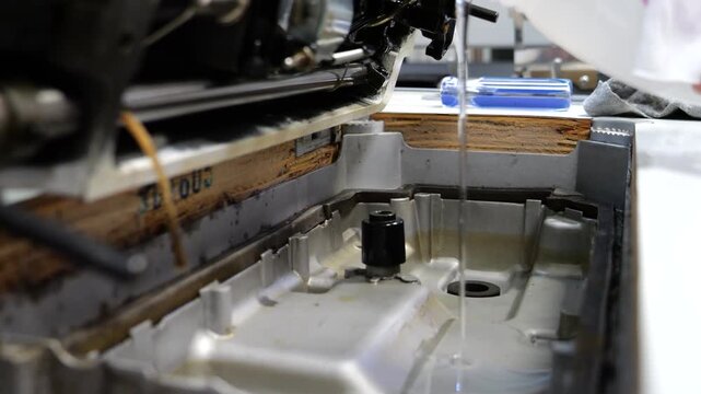 Male hand adding new oil to a professional sewing machine.. Machine maintenance 4k 60 frame video close up.