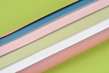 Fototapeta premium Top view of several overlapping layers of pastel colored plastic sheets in pink blue and white arranged diagonally over a solid green surface for creative background