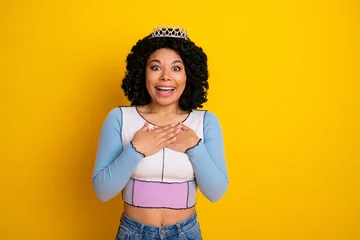 Fotobehang Onderzeeër Happy young woman in casual trendy outfit with crown against yellow background expressing joy and surprise  © deagreez