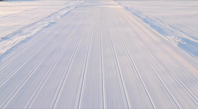 A low-angle perspective shot reveals multiple perfectly parallel ski or snowmobile tracks imprinted on a pristine, freshly fallen snow surface under diffused natural light.