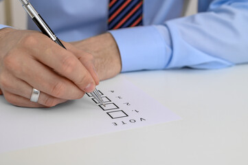 An elegantly dressed man in a shirt and tie checks a box on a ballot paper.