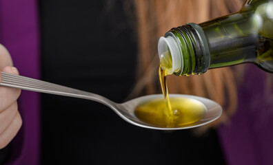 Close-up of golden olive oil being poured onto a spoon straight from the bottle