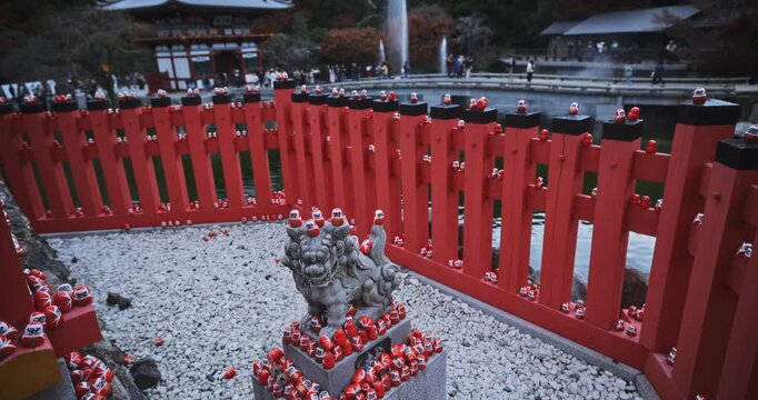 Medium steady cam rising shot on ancient stone beast surrounded by small daruma dolls at shrine