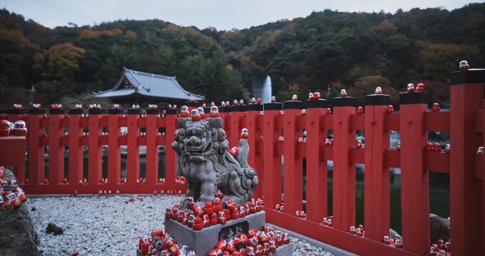 Little daruma dolls on ancient stone creature behind Japanese gate - steady cam shot