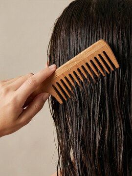 Woman combs wet hair with wooden comb in indoor setting