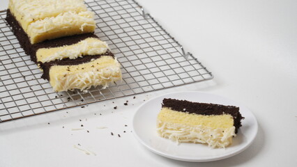 Steamed chocolate vanilla sponge cake topped with grated cheddar cheese served using a cooling rack placed in a white place (isolated white).