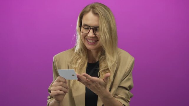 Young woman holding a card smiles against a vibrant pink background, showcasing a modern and cheerful interaction with digital payment methods and finance in an isolated setting.