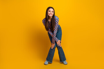 Obraz premium Young stylish Latina teen smiling in a yellow studio wearing a patterned top and jeans in a casual fashion shoot