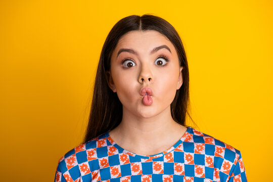 Young brunette girl creates playful kiss face against a bright yellow background wearing a bold patterned shirt for a fun lifestyle stock image