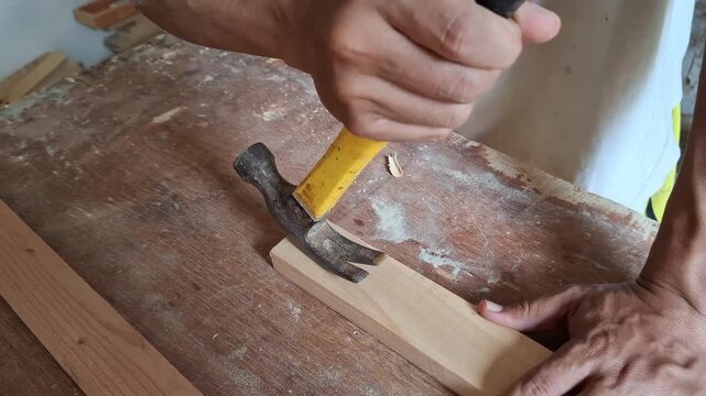 A carpenter using a hammer to took nail from wooden board.
