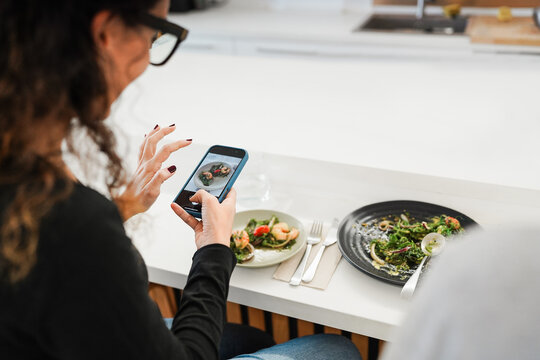 Food influencer woman eating lunch while making photo of dish with smartphone in trendy bar restaurant - Healthy lifestyle, technology and social media trends concept - Focus on female left hand