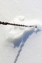 A rusty ship chain from a pier, frozen into the ice on a winter river.