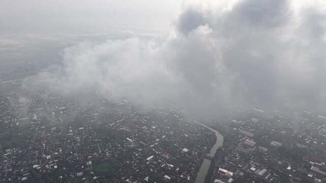 Aerial View Over Dense City With River, Clouds, And Urban Landscape From Airplane Window