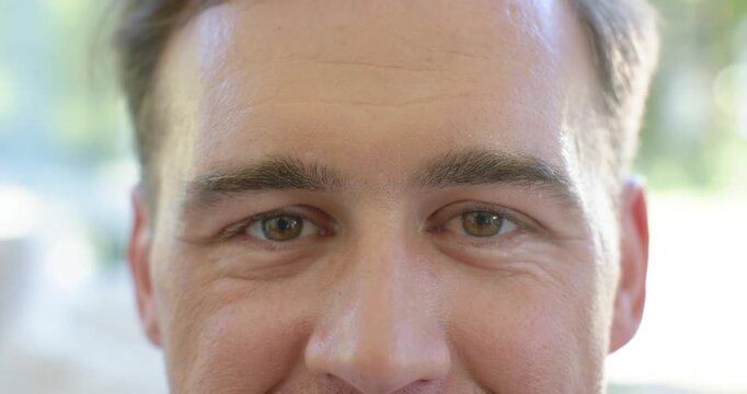 Man holding gaze to camera in bright room, blinking and smiling, signaling warmth with window light