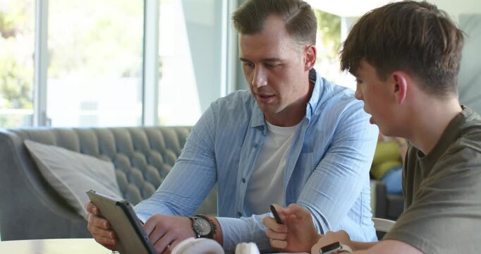Male mentor and youth at home, mentor pointing at tablet, teaching while youth asking with stylus