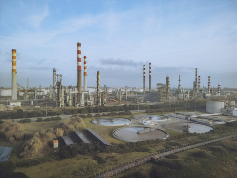Aerial view of an industrial complex with towering chimneys piercing the skyline, juxtaposed against circular tanks and green patches, Matosinhos, Portugal.