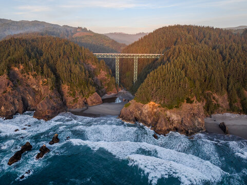 Aerial view of the Thomas Creek Bridge stands tall amidst the rugged coastline, where the forest meets the turbulent ocean, Brookings, Oregon, United States.