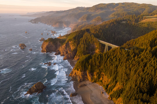 Aerial view of the rugged coastline where the forest meets the sea, a bridge standing as a testament to human engineering against the natural beauty, Brookings, Oregon, United States.