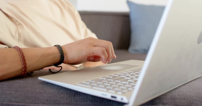 Hands with braided bracelets are typing on silver laptop on sofa, shifting and pausing to rest