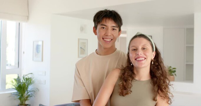 Asian man holding woman olive top, woman turning laughing, sharing, facing camera in apt with plant