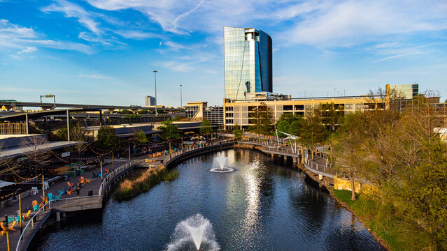 Aerial view of the glassy high-rise tower reflecting the sky, standing tall over the waterway and adjacent boardwalk, Plano, Texas, United States.