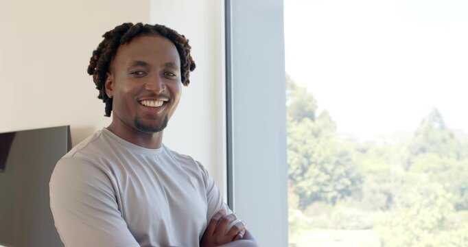 Adult African male in gray shirt standing by window TV noticing camera turning smiling, copy space