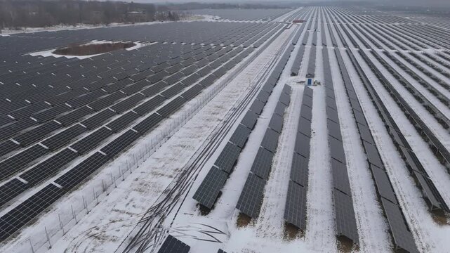 Drone footage of a large photovoltaic park near Leipzig, Germany. Snow-covered panel rows and service roads create strong linear patterns across a wide winter landscape.