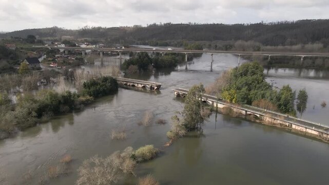 Aerial footage circles the collapsed bridge approach, revealing a deep cavity where floodwater erosion removed the supporting soil beneath the roadway. Drone rotating to the left.