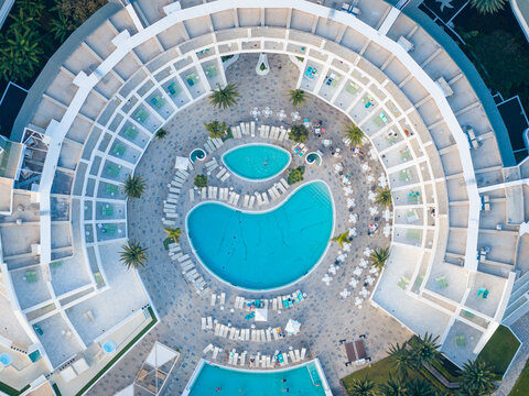 Aerial view of a luxury resort's concentric architecture encircling turquoise pools and sunbeds under the bright sun, Playa Blanca, Lanzarote, Canary Islands.